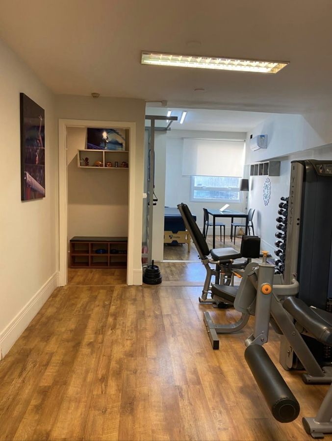 Corredor da clínica com os aparelhos de musculação ao fundo.