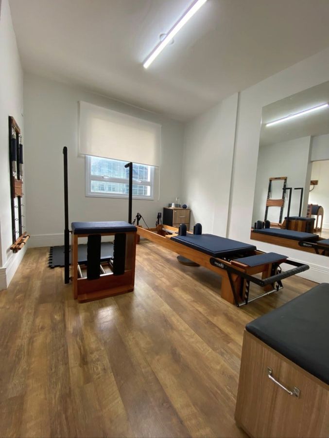 Estúdio de Pilates, com cadeira, reformer e espelho.