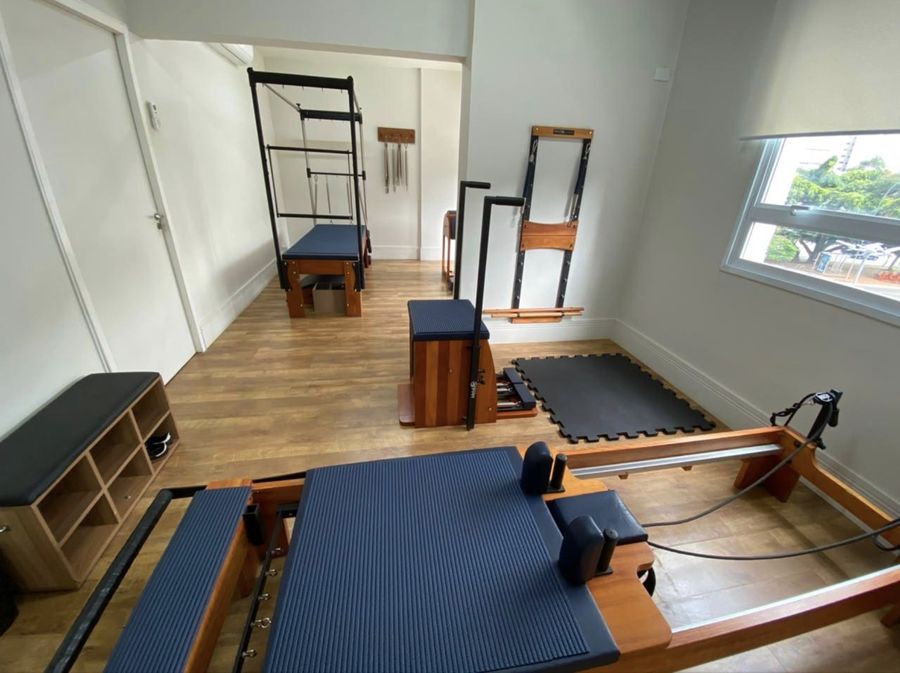 Vista geral do estúdio de Pilates, com reformer, cadillac e cadeira.