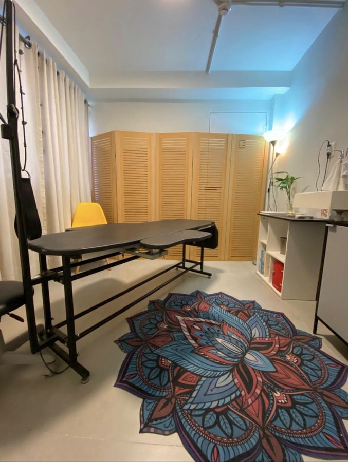 Sala reservada de fisioterapia, com maca e biombo.