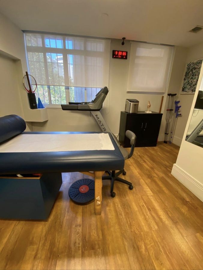 Sala de fisioterapia com maca, esteira e equipamentos de apoio à marcha.